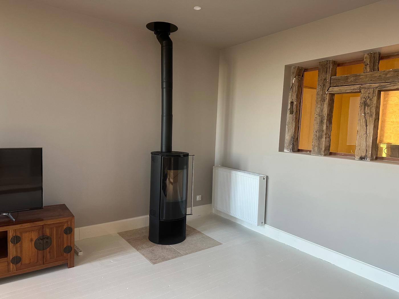 Poêle à bois cylindrique avec conduit noir et plaque de sol en pierre